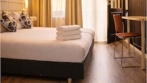 Een hotelkamer met een bed, een stoel, een aan de muur bevestigde televisie en een raam met gordijnen.