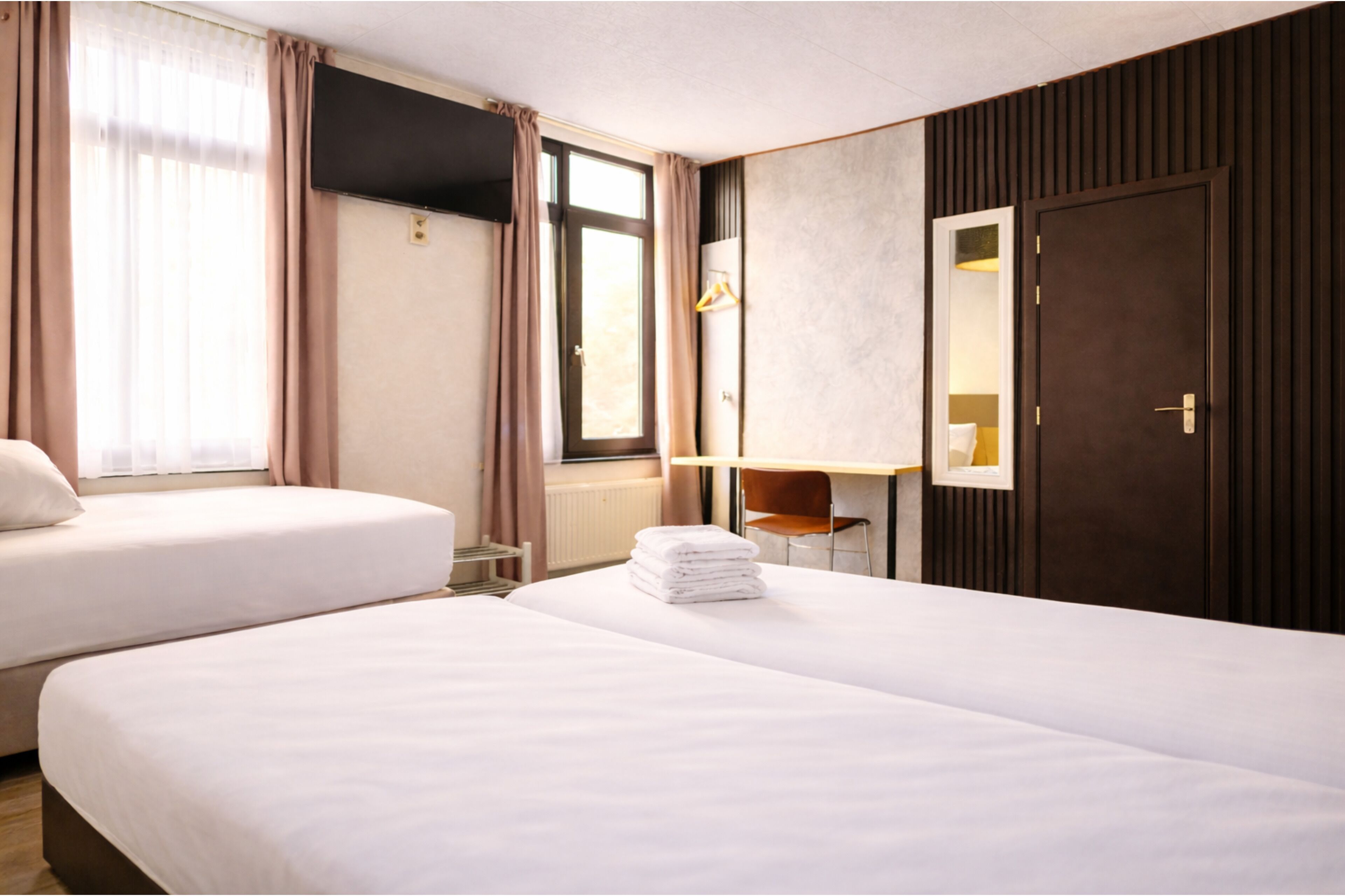 Une chambre d’hôtel avec deux lits, un bureau, une chaise, un miroir et une fenêtre avec des rideaux.