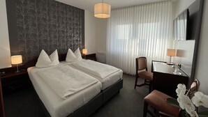 A hotel room with a double bed, a desk with a chair, a TV, and a large window with sheer curtains. - Hotel Garni Geisler (Cologne)