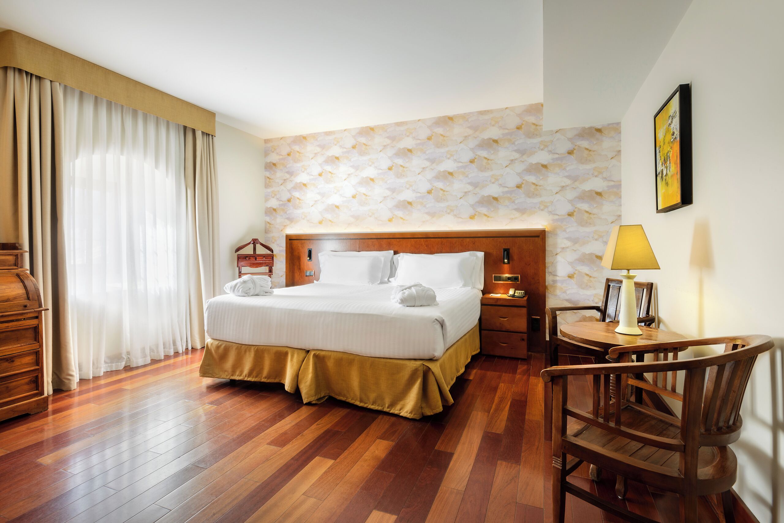 Habitación de hotel con una cama y mesita de noche de madera, un escritorio con lámpara y una silla.