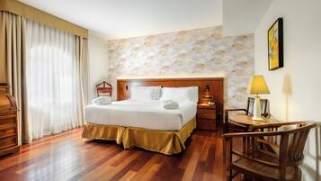 Habitación de hotel con una cama y mesita de noche de madera, un escritorio con lámpara y una silla.