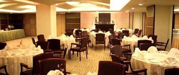 Un salón de banquetes con mesas redondas dispuestas para comer, sillas alrededor de cada mesa y un escenario al fondo.