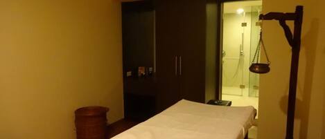 A room with a bed, a wooden cabinet, a scale, and a trash bin.