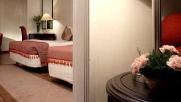 A hotel room with a bed, a nightstand, a lamp, a red chair, and a vase with flowers.