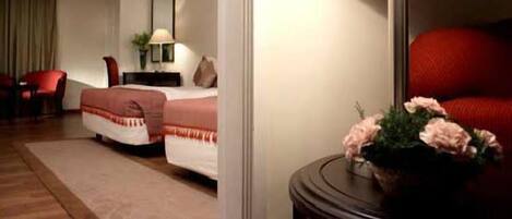 Una habitación de hotel con una cama, una mesita de noche, una lámpara, una silla roja y un jarrón con flores.