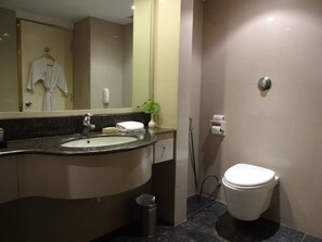 Un baño moderno con lavamanos, espejo, inodoro y una bata colgada.