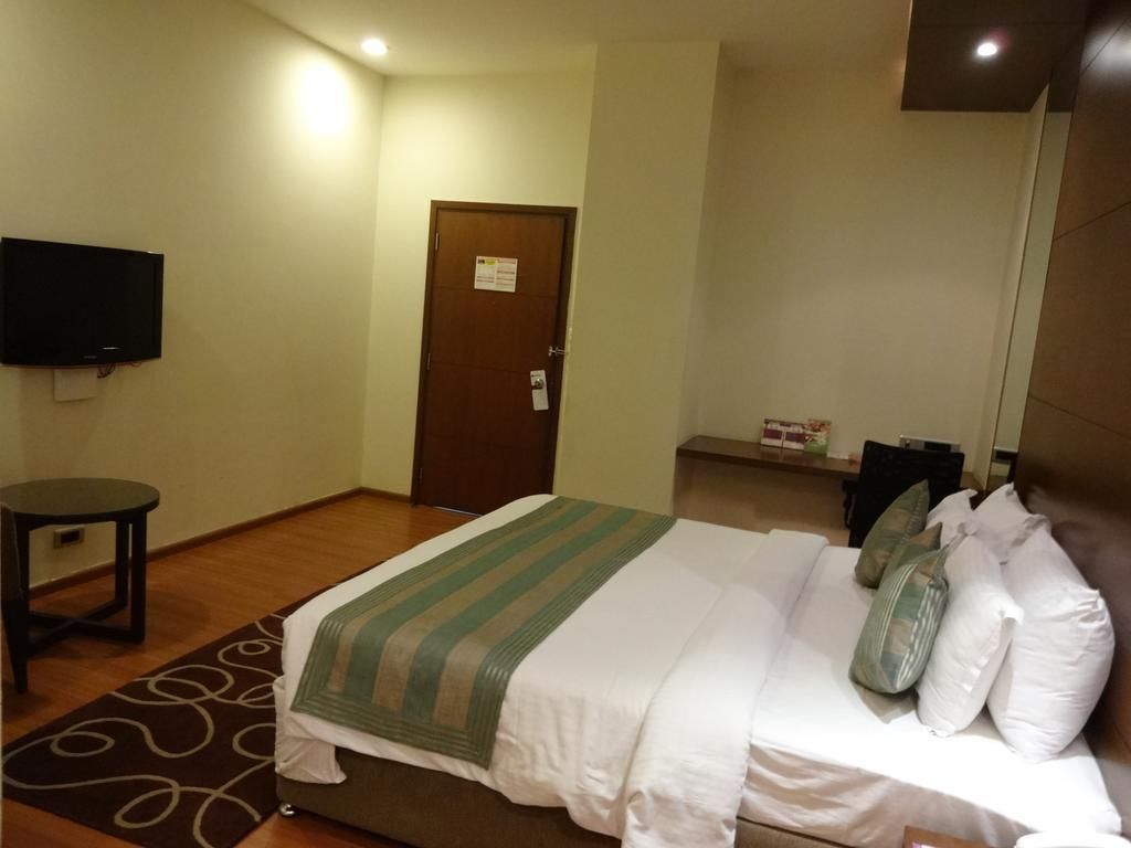 Una habitación de hotel con una cama, televisión, puerta y una mesita.