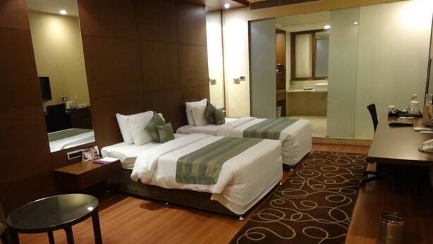 A hotel room with two beds, a small table, a mirror, and a bathroom visible through an open door. - Minerva Grand Secunderabad (Hyderabad)