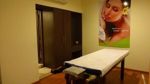 A treatment room with a massage table, a poster on the wall, and a door leading to a storage area. - Minerva Grand Secunderabad (Hyderabad)
