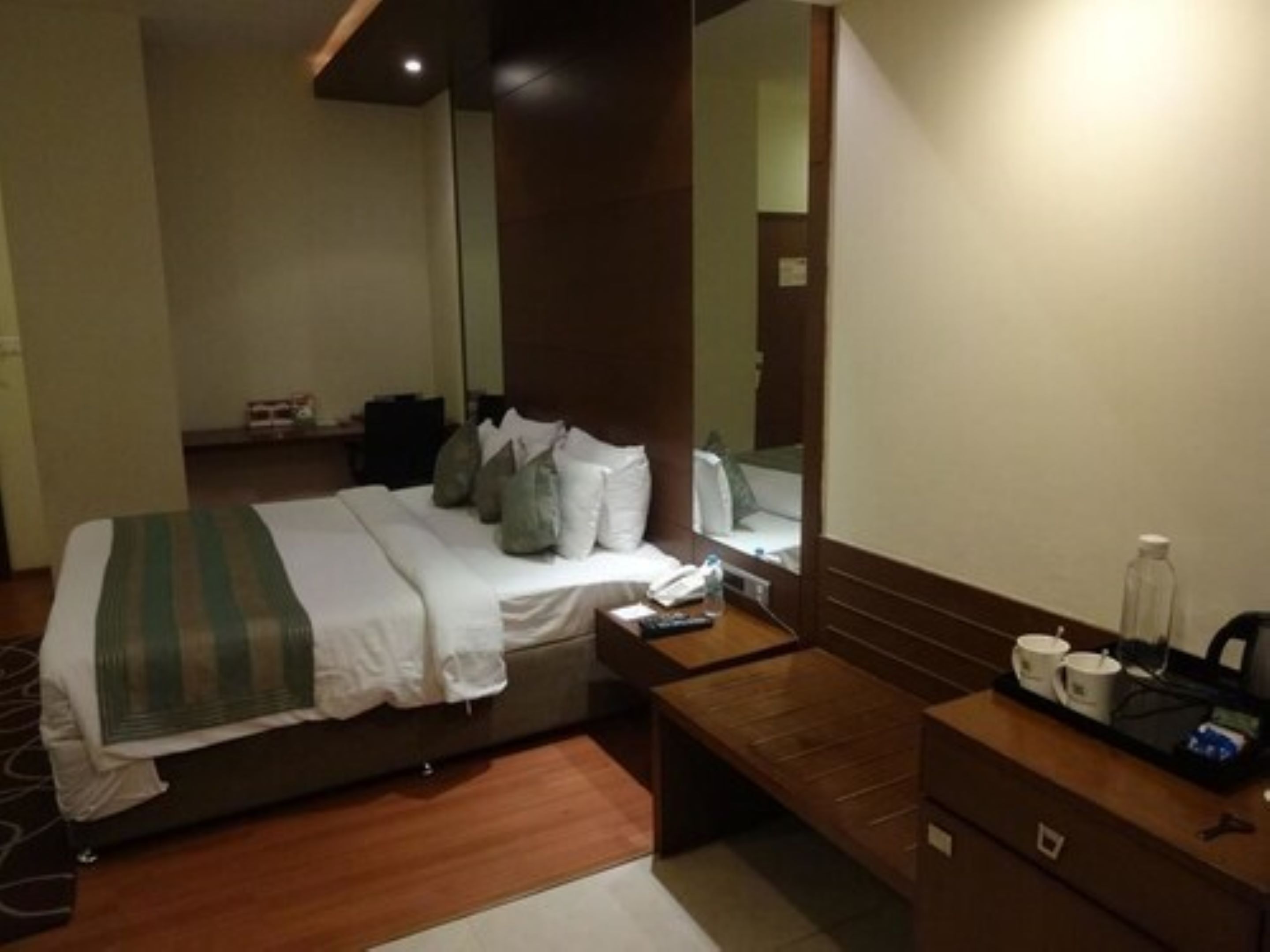A hotel room with a bed, bedside table, and a mirror.