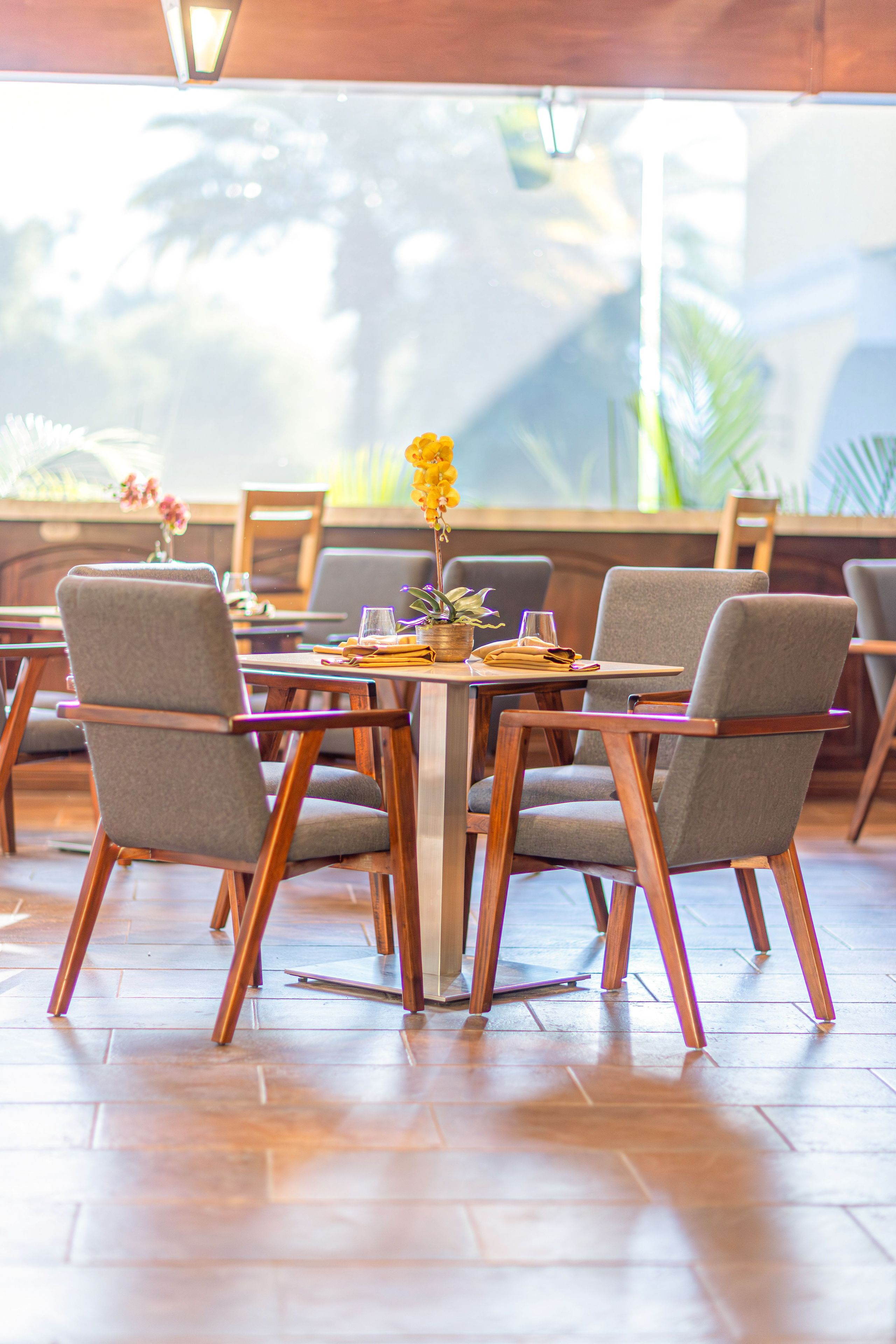 Un restaurante con mesas y sillas de madera, un jarrón con flores y vistas al exterior.