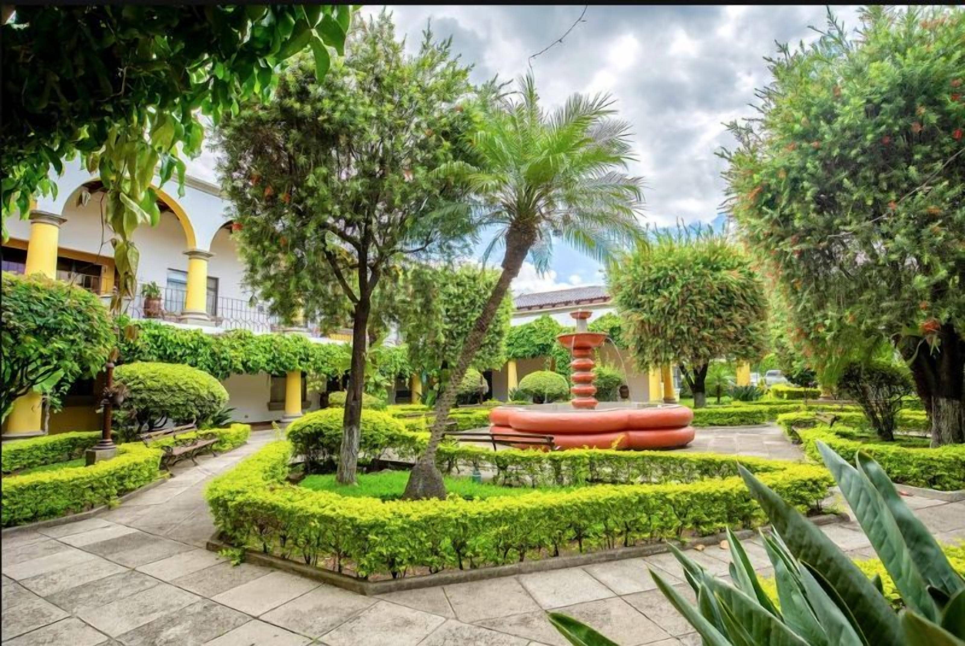 A courtyard with a fountain, trimmed hedges, and a pathway.