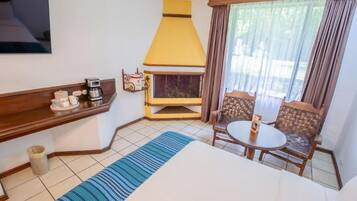 A hotel room with a bed, a coffee maker, a fireplace, a TV, and a window with curtains.