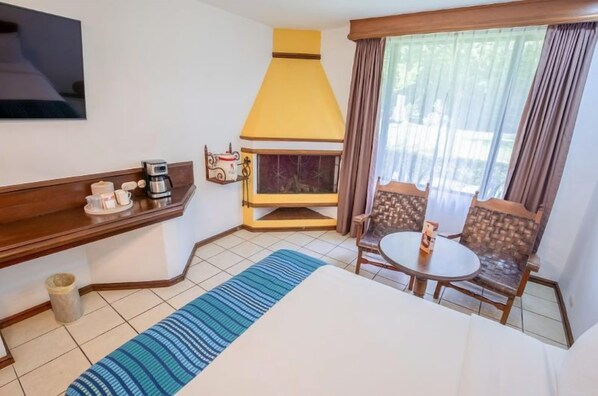 Una habitación de hotel con cama, cafetera, chimenea, televisor y ventana con cortinas.