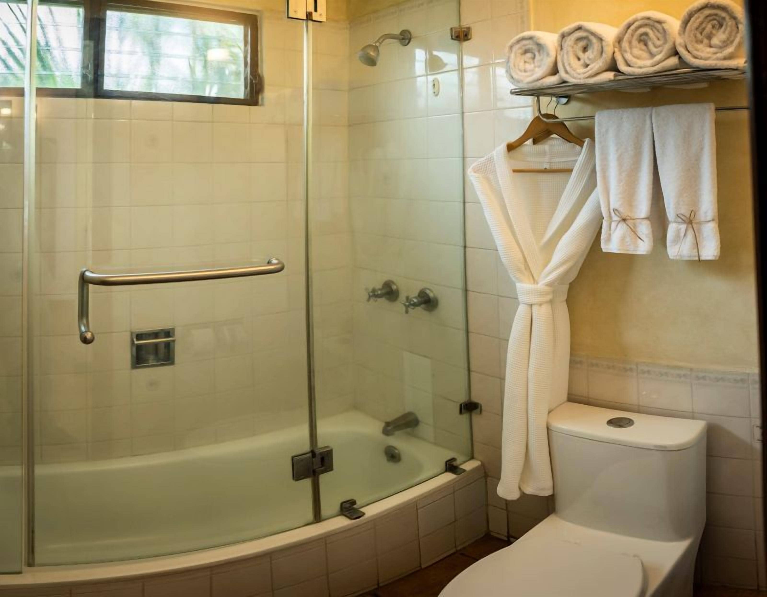A bathroom with a glass-enclosed shower, a bathtub, and a toilet. There are towels and a robe hanging on a rack.