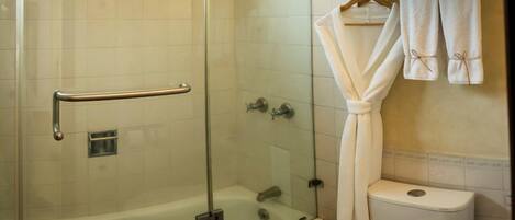 A bathroom with a glass-enclosed shower, a bathtub, and a toilet. There are towels and a robe hanging on a rack.