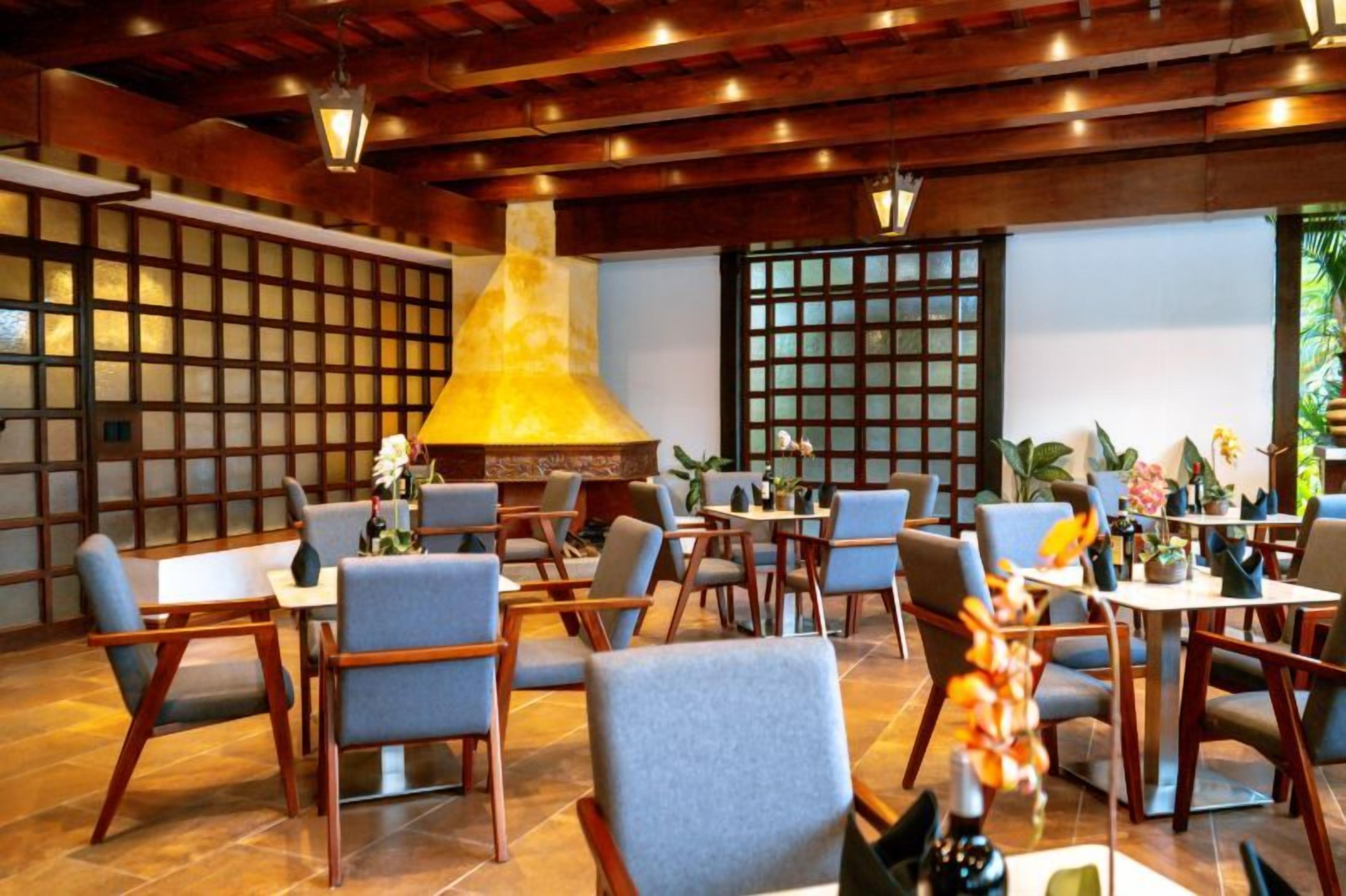 Un restaurante con vigas de madera, una lámpara central grande y mesas con sillas.