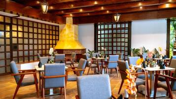 A restaurant with wooden beams, a large central light fixture, and tables with chairs.