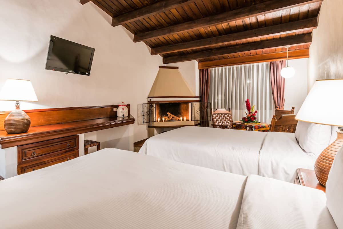 A hotel room with two beds, a flat-screen TV, a fireplace, and a wooden ceiling.
