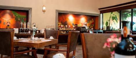 A restaurant with wooden tables and chairs, a coffee station, and a mural on the wall.