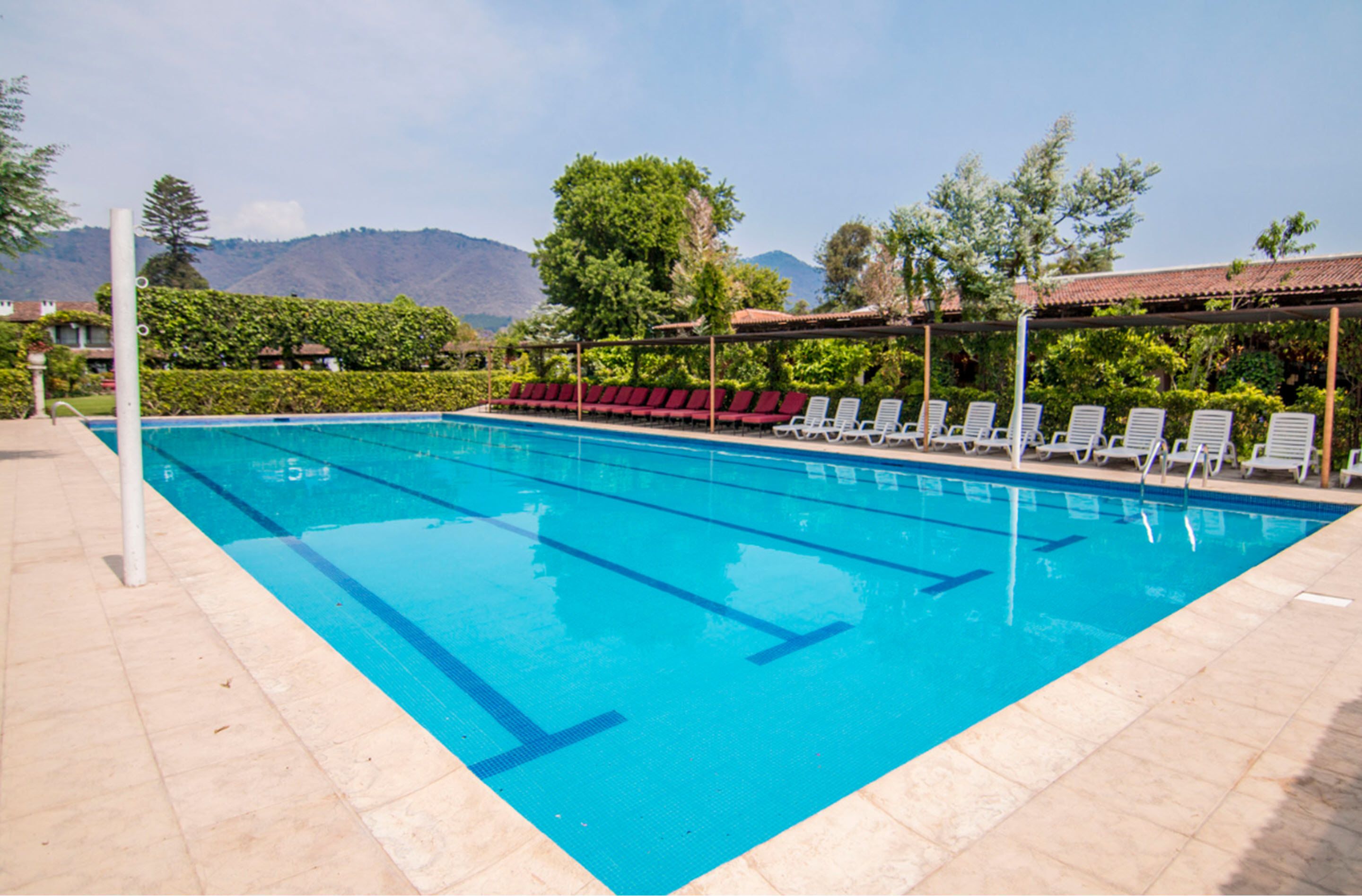 Una piscina con agua azul cristalina, rodeada de sillas de descanso y una terraza con baldosas.