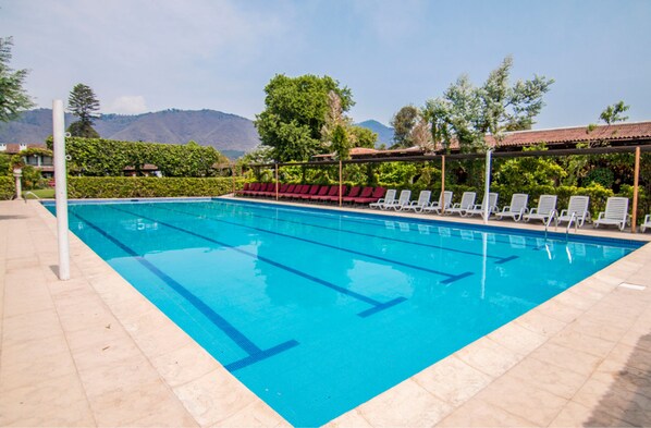 A swimming pool with clear blue water, surrounded by lounge chairs and a tiled deck.