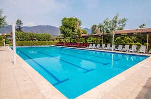 Una piscina con agua azul cristalina, rodeada de sillas de descanso y una terraza con baldosas.