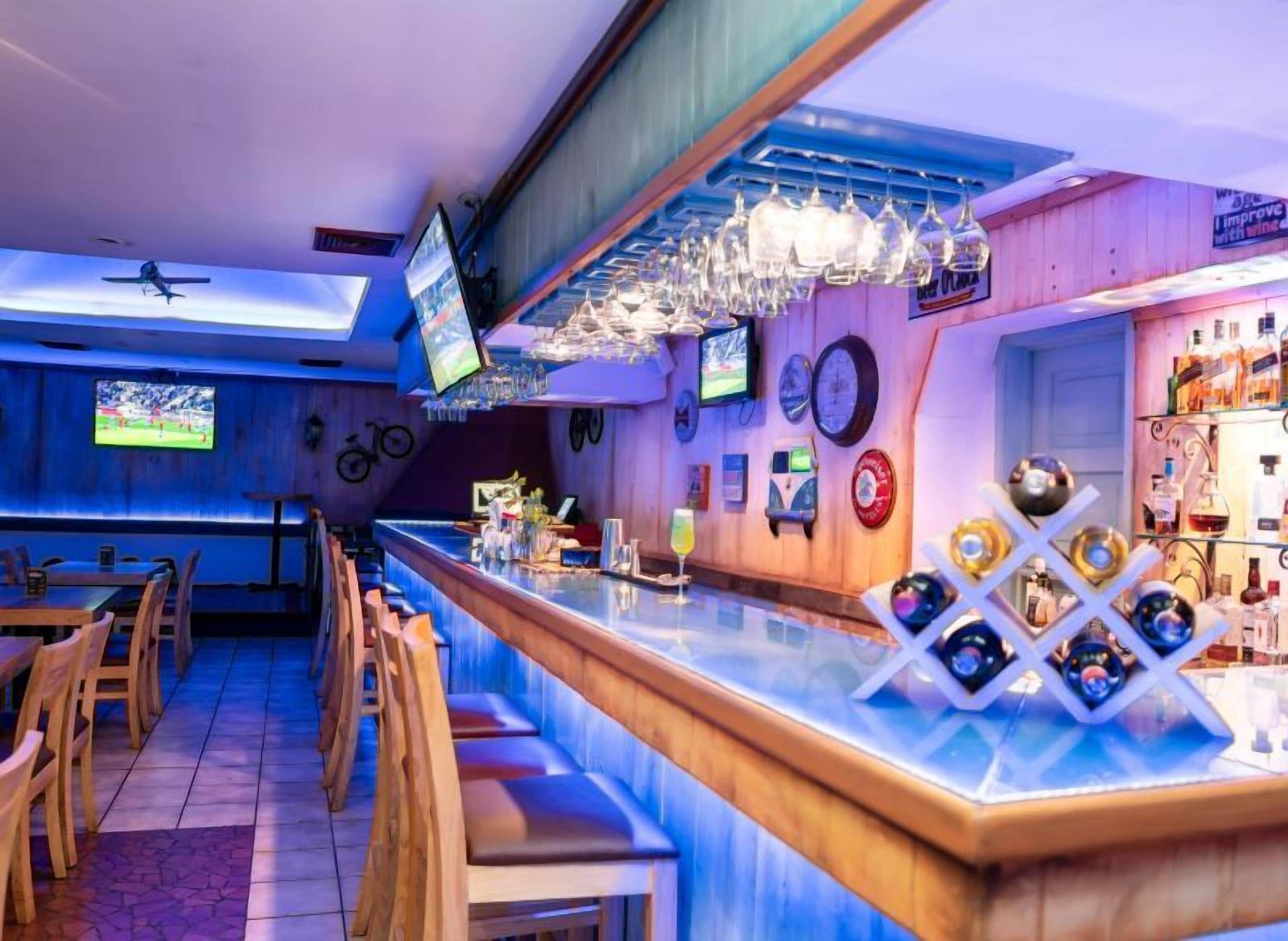A bar area with a long counter, bar stools, and a television screen.