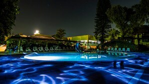 Ein Poolbereich bei Nacht mit Wasserrutsche, Liegestühlen und einem Gebäude im Hintergrund.
