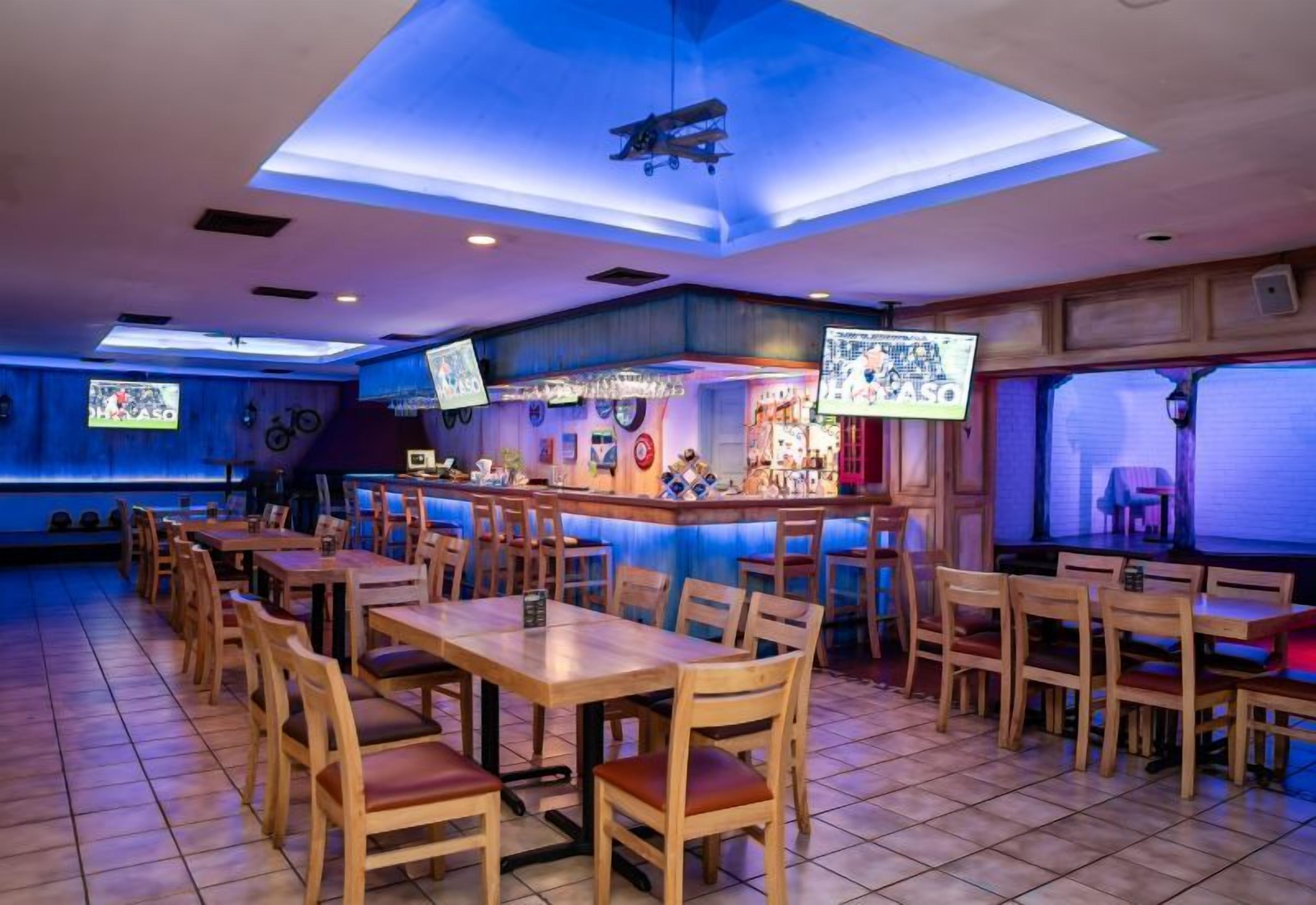 A restaurant with multiple wooden tables and chairs, a bar area, and a ceiling with a skylight.