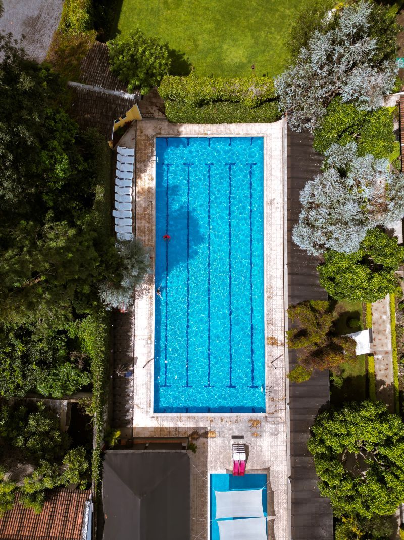 An aerial view of a rectangular swimming pool surrounded by greenery and a wooden deck.