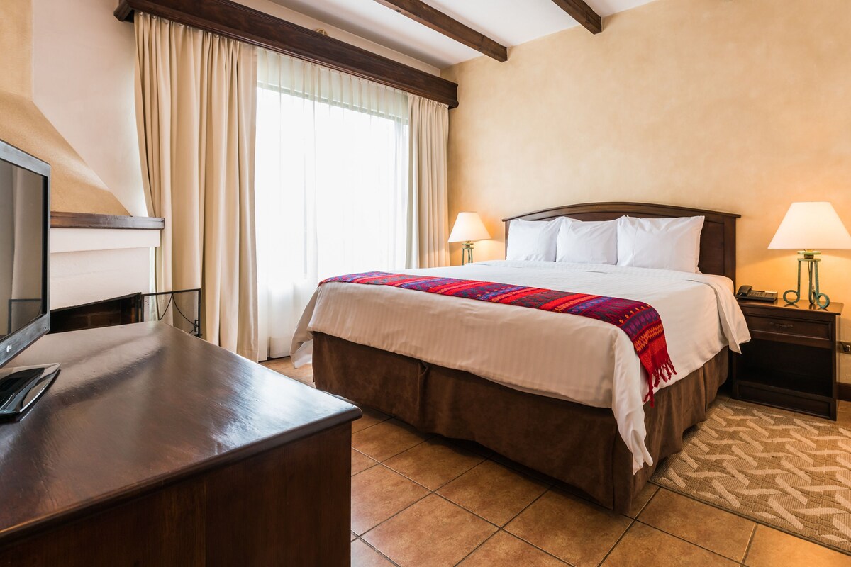 Una habitación de hotel con una cama, dos lámparas de noche, un escritorio con una computadora y un televisor.