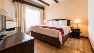 Una habitación de hotel con una cama, dos lámparas de noche, un escritorio con una computadora y un televisor.