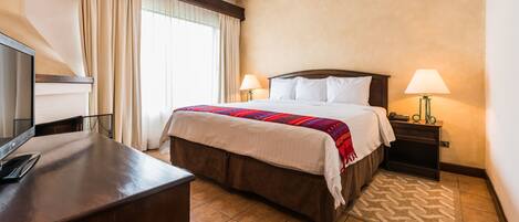 Una habitación de hotel con una cama, dos lámparas de noche, un escritorio con una computadora y un televisor.
