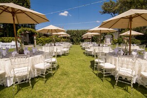 An outdoor wedding venue with rows of white tables and chairs, each under a large umbrella.
