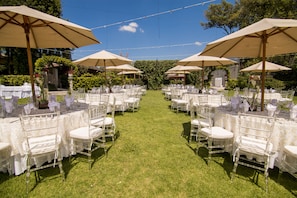 An outdoor wedding venue with rows of white tables and chairs, each under a large umbrella.