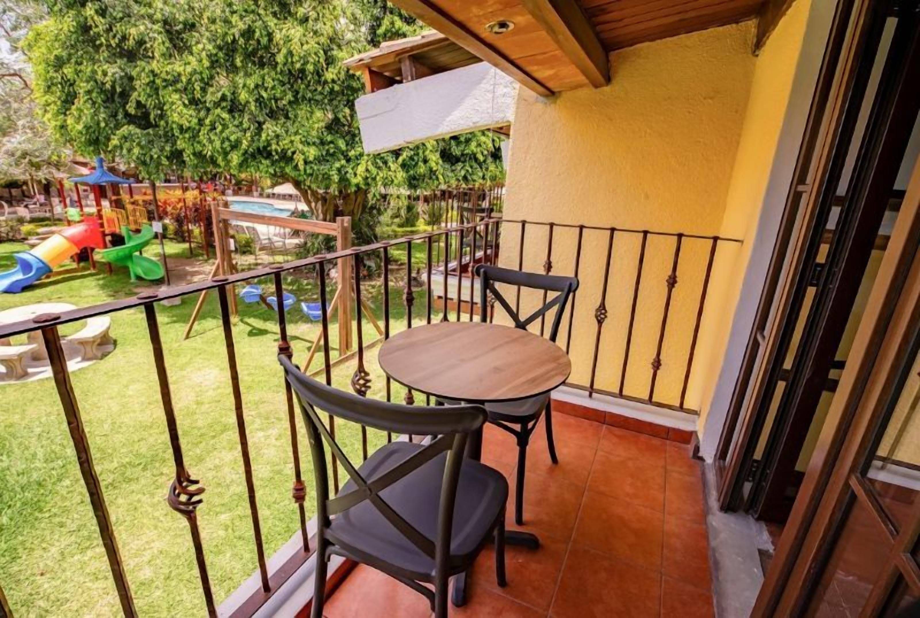 Ein Balkon mit Tisch und Stühlen, Blick auf einen Spielplatz und ein Schwimmbecken.