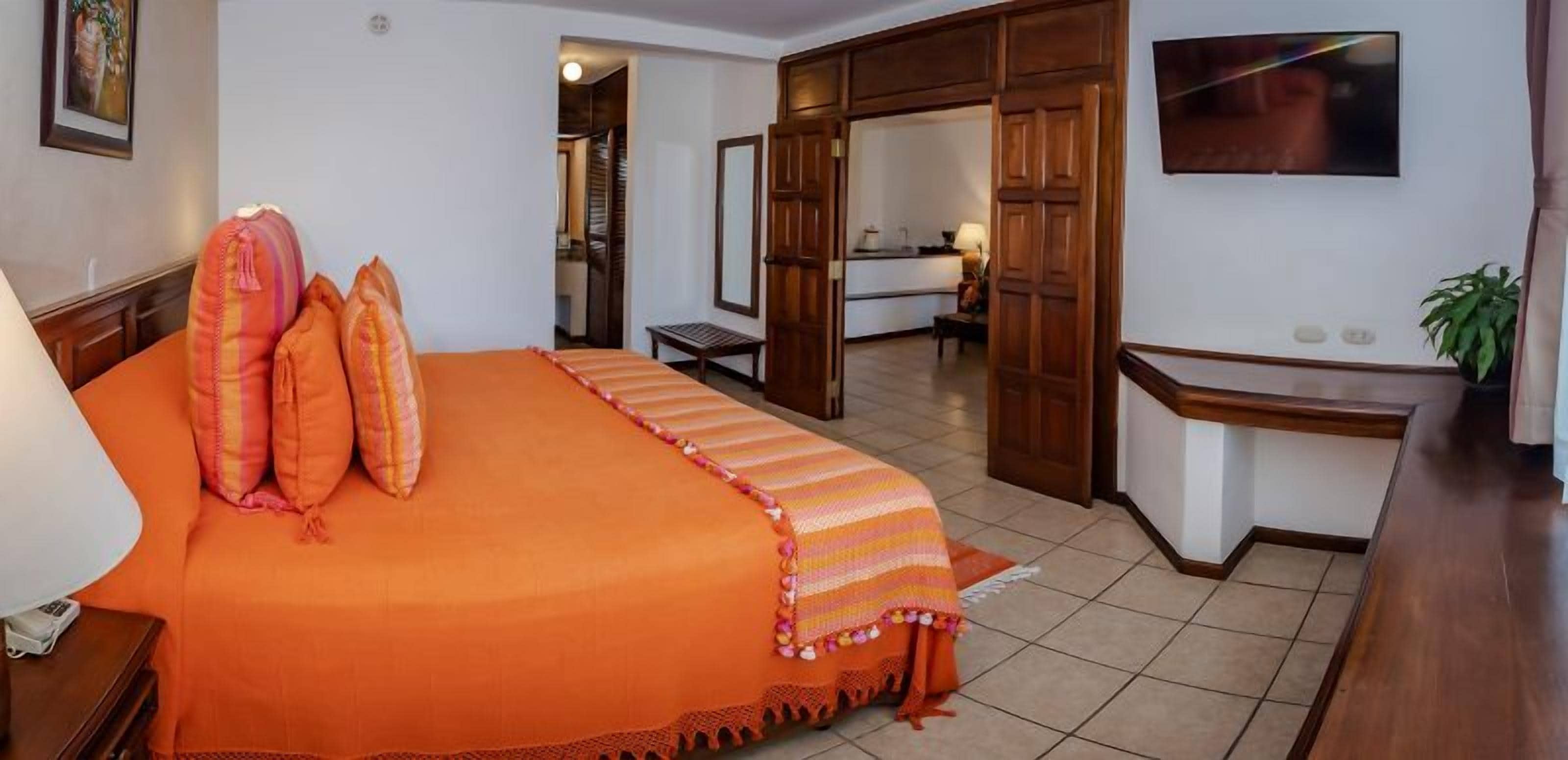 A hotel room with a large bed, a desk, a television, and a bathroom visible through an open door.