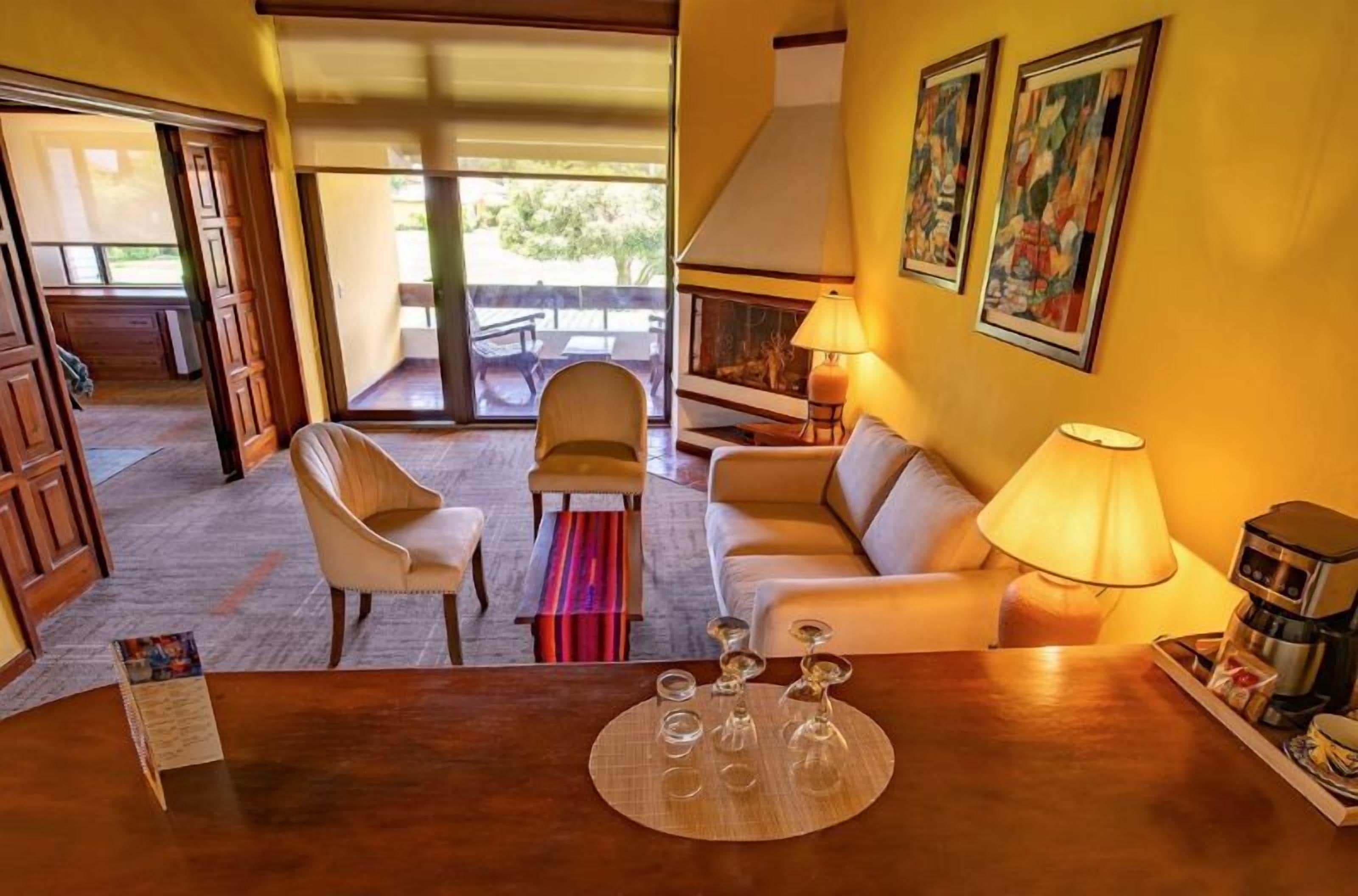 Habitación de hotel con sofá, sillas, una mesa de centro y una mesa de comedor con lámpara.
