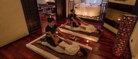 A room with wooden flooring, a massage table, a massage therapist, and a bathtub.