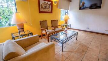 Una sala de estar con sofá, sillas, una mesa de centro y un televisor en la pared.