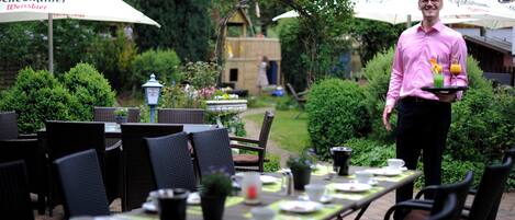 Un área de comedor al aire libre con mesas dispuestas para los huéspedes, rodeada de follaje y sombrillas.