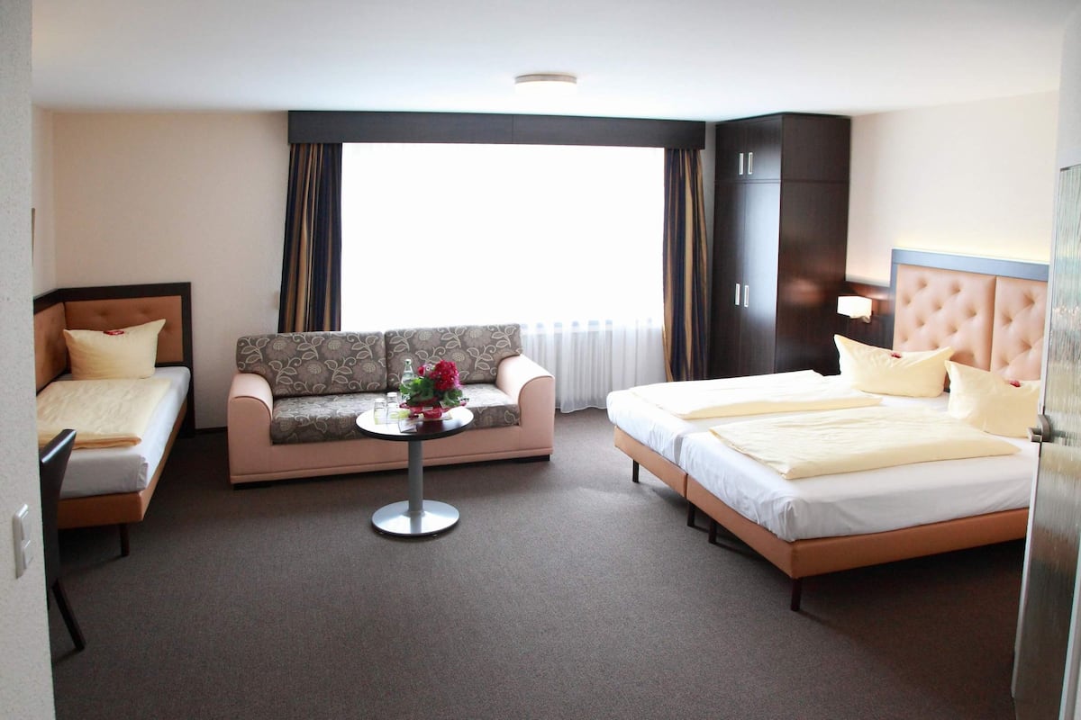 A hotel room with a bed, a sofa, and a small table with flowers.