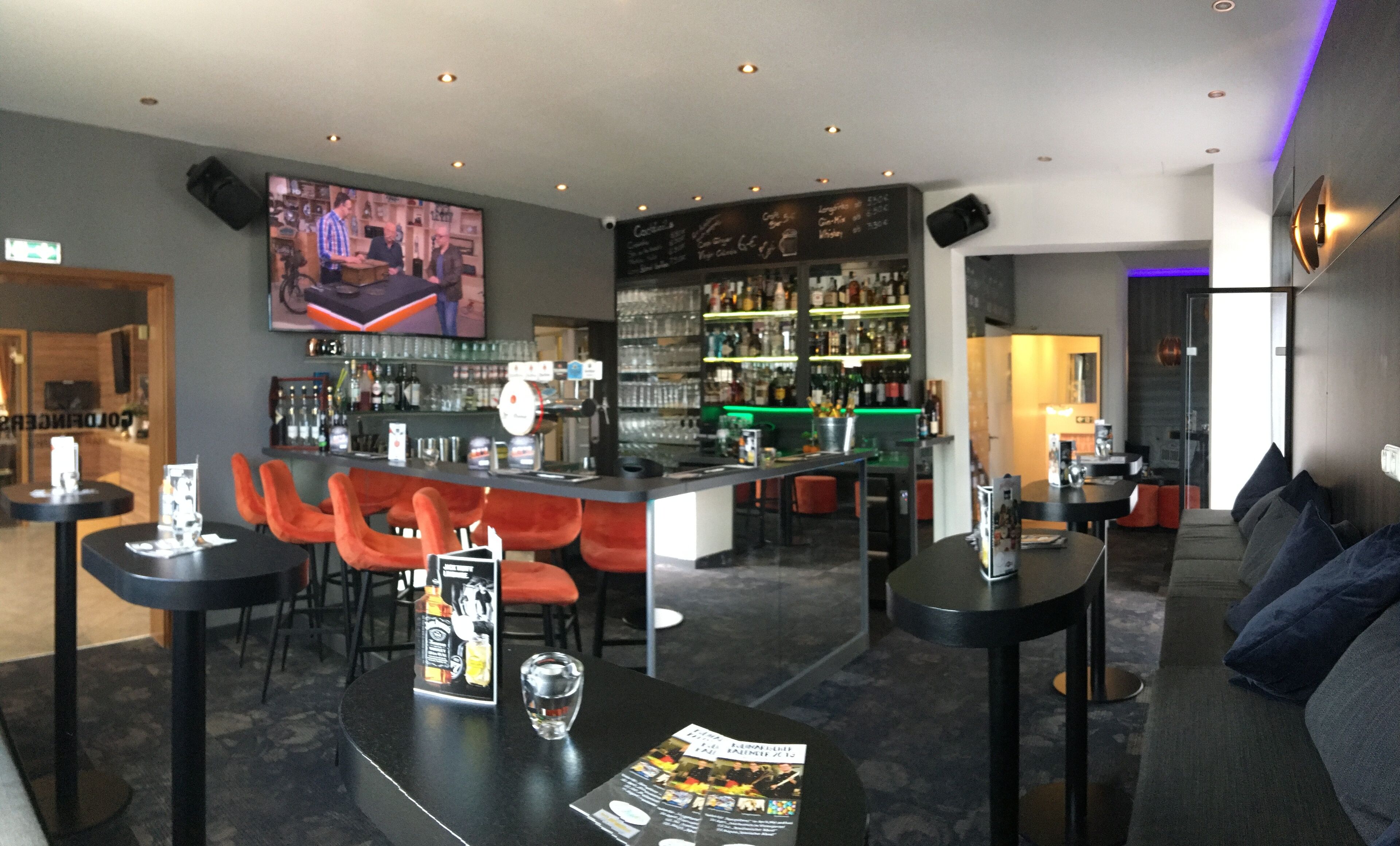 A bar area with red chairs, a counter with a menu, and shelves stocked with bottles.
