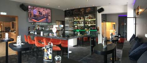 A bar area with red chairs, a counter with a menu, and shelves stocked with bottles.