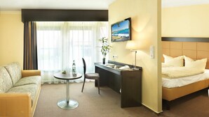 A hotel room with a bed, a desk, a chair, a small table, and a TV on the wall. - Hotel zur Heidebluete (Hambuehren)