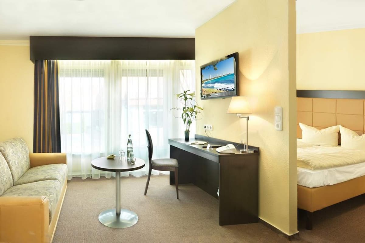 A hotel room with a bed, a desk, a chair, a small table, and a TV on the wall.