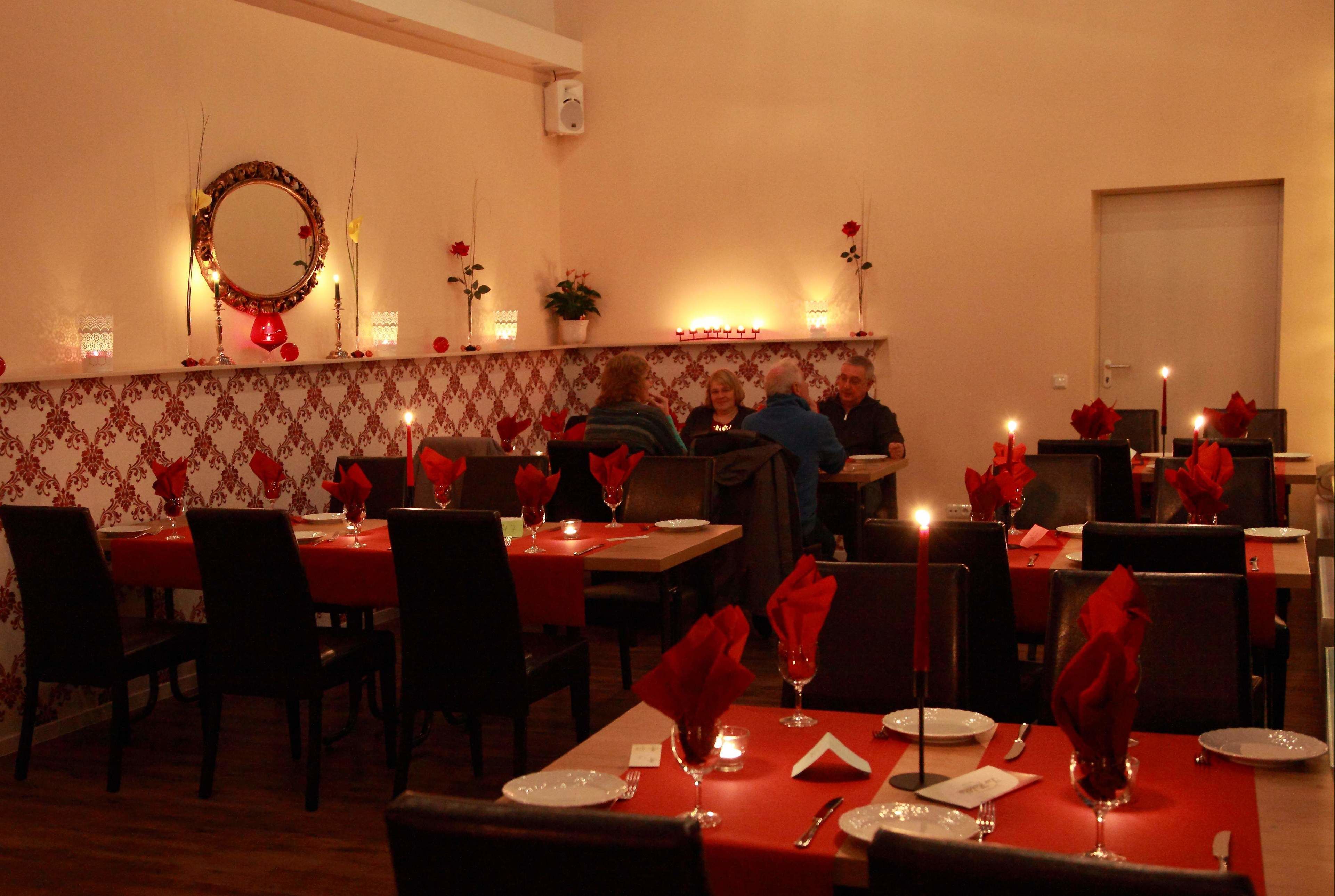 A restaurant with tables set for dining, featuring red napkins, candles, and a mirror on the wall.