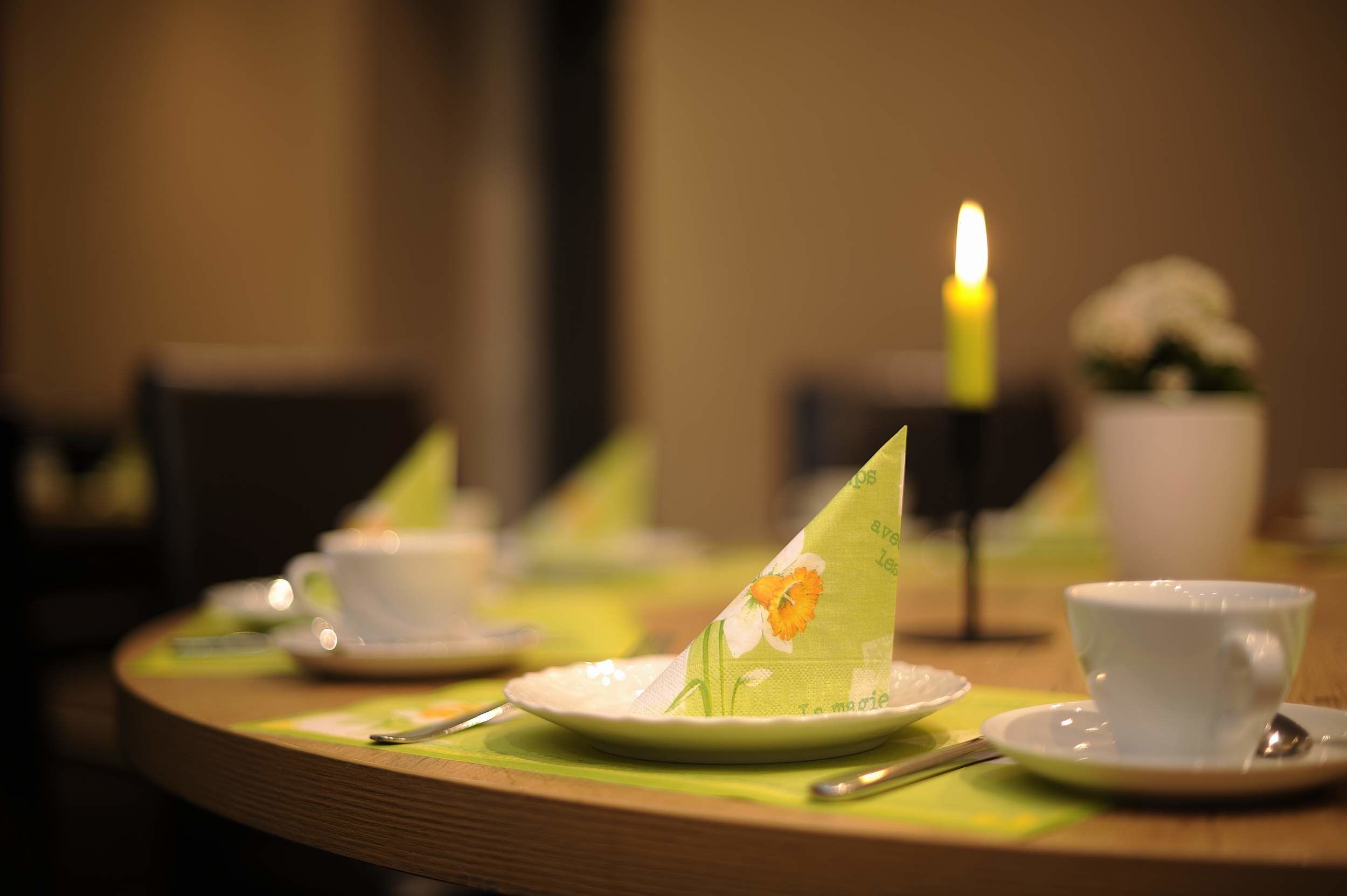 A dining table with a candle, a flower, and a cup.