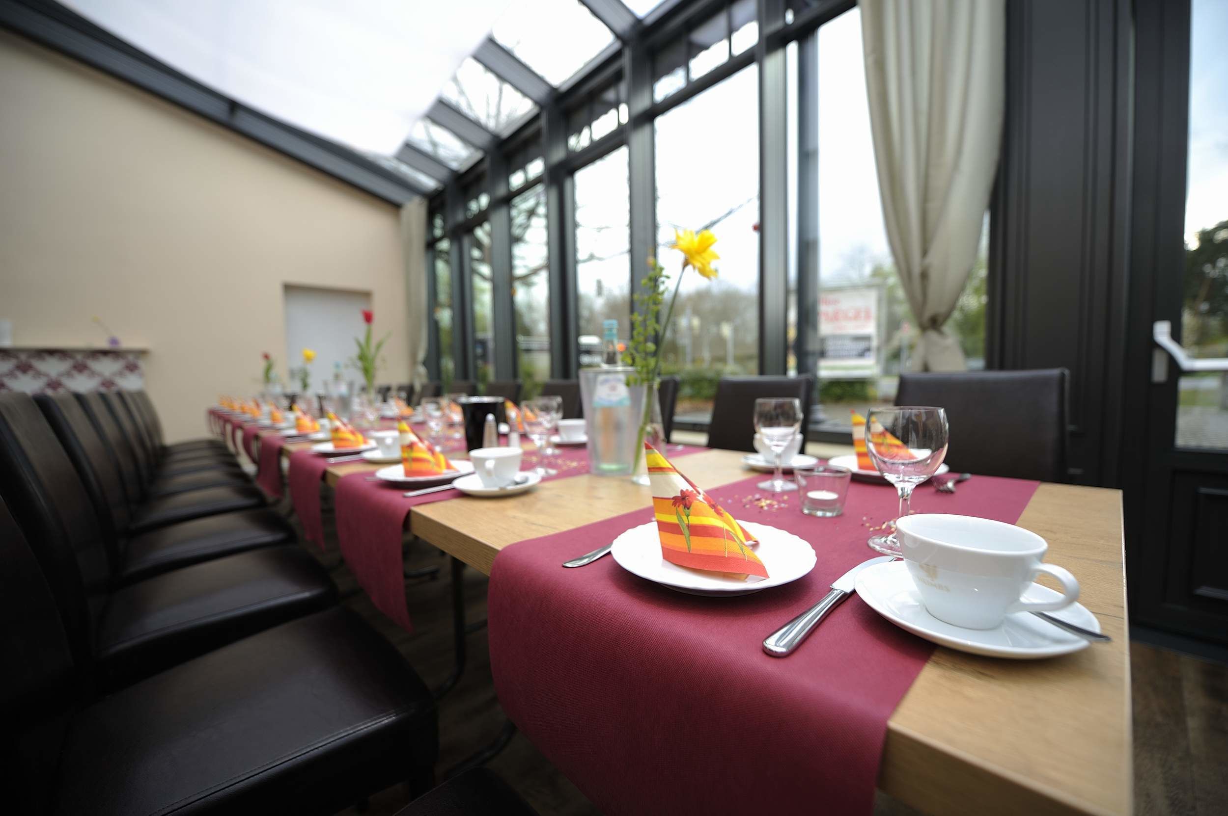A dining area with a long table set for a meal, featuring a red tablecloth, white plates, and a glass of water.